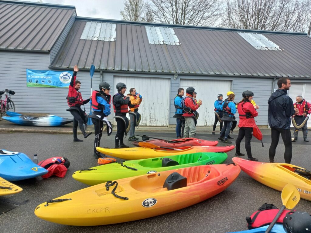 Groupe de kayakistes debout en tenue en train de s'échauffer. Leur kayaks sont posés au premier plan.